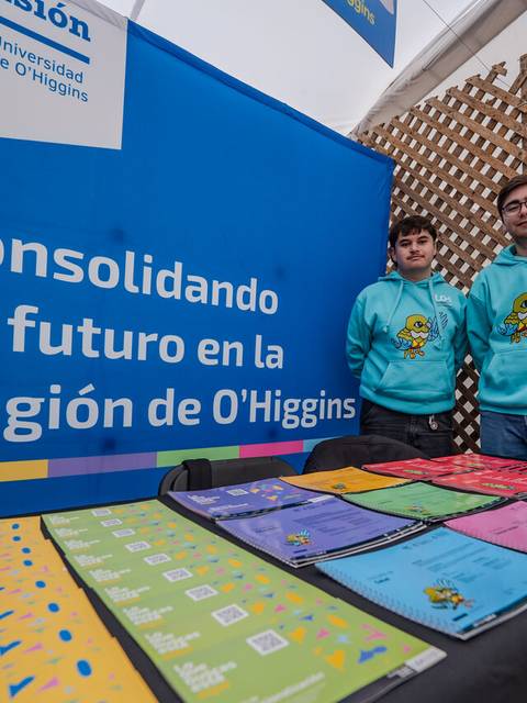 Dos jóvenes posan frente a un stand de la Universidad de O'Higgins con productos en una feria.
