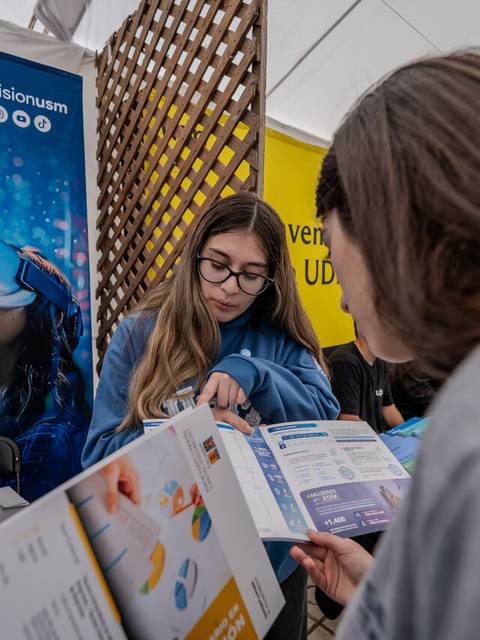 Una estudiante informando sobre programas académicos en una feria educativa.