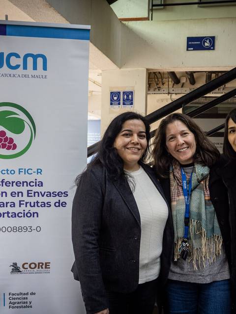 Tres mujeres sonrientes junto a un banner de un proyecto universitario en Chile.