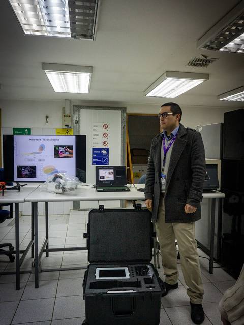 Un hombre presenta un equipo técnico en un laboratorio con computadores y pantallas.