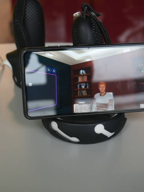 Un celular está mostrando una persona virtual sentada en un entorno digital.