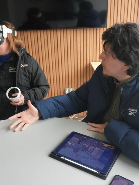 Una mujer con gafas de realidad virtual interactúa mientras un hombre le explica algo en una mesa.