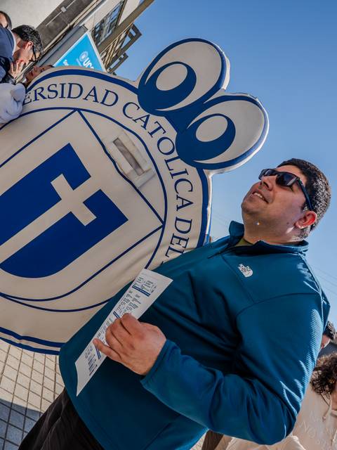 Un hombre sostiene un folleto junto a una figura que representa la Universidad Católica de Chile.