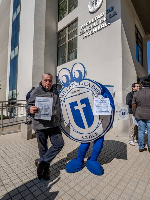 Un personaje disfrazado y un hombre sosteniendo papeles frente a la Facultad de Ciencias de la Ingeniería en la Universidad Católica de Chile.