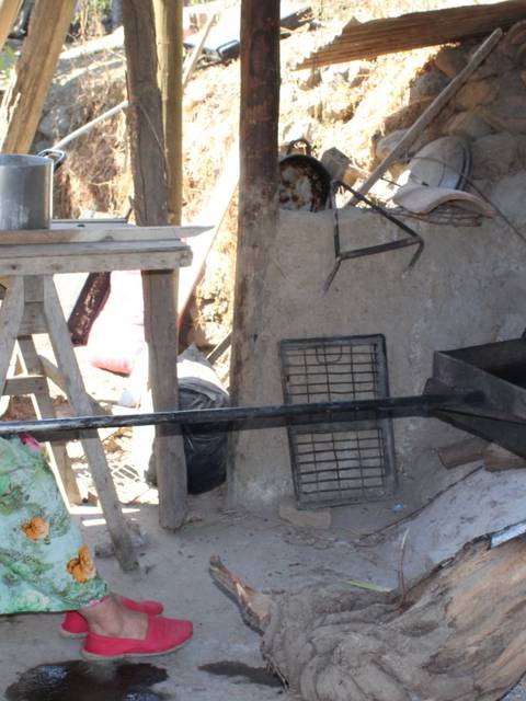 Una mujer en un entorno rural está cocinando al aire libre con una olla sobre el fuego.
