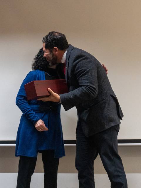 Dos personas se abrazan en un escenario mientras una de ellas sostiene una caja en las manos.