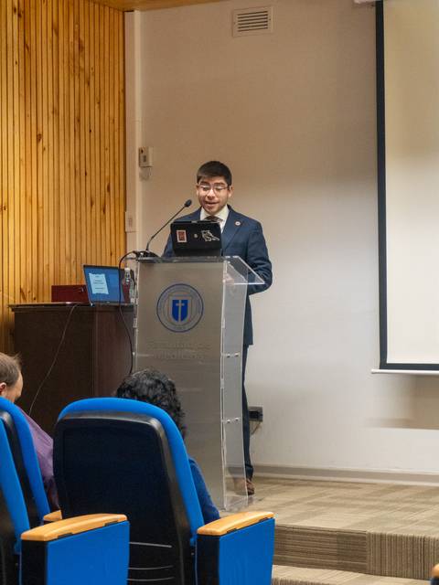 Un joven exponiendo en una conferencia con un proyector detrás.