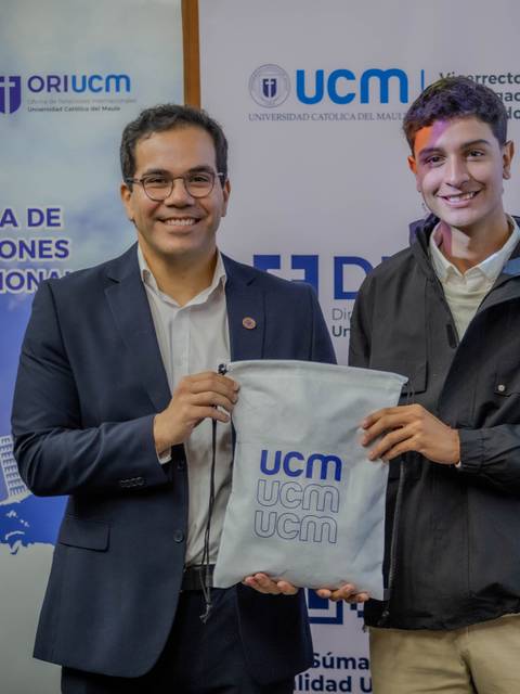 Dos personas posando con una mochila de la UCM en un evento de relaciones internacionales.