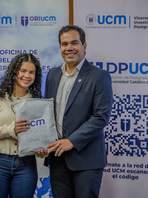 Dos personas posan sonrientes mientras sostienen un objeto en un evento de la universidad.