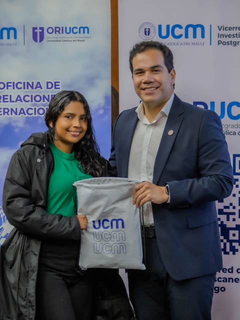 Un estudiante sonriente recibe un obsequio de la UCM de manos de un representante en una ceremonia.