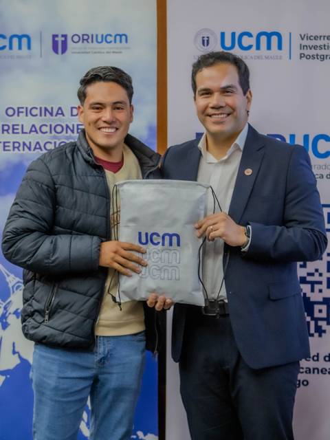 Dos personas posando con una mochila de la UCM en un evento oficial.