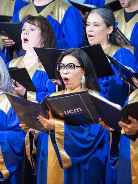 Un coro con personas vestidas de azul y dorado, cantando con gran emoción.
