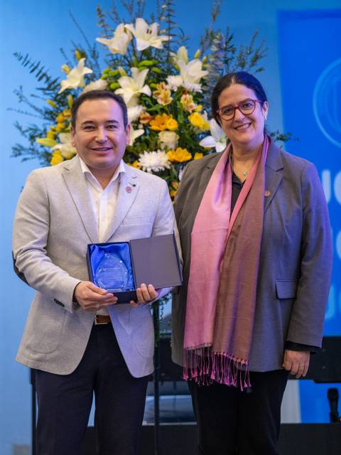 Una pareja de personas sonríe mientras sostienen un premio en un evento de reconocimiento.