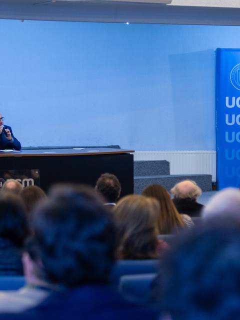 Un evento académico en la UCM con un orador frente a un público atento.