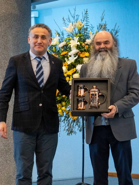 Dos hombres posando con un regalo en un evento que parece formal.