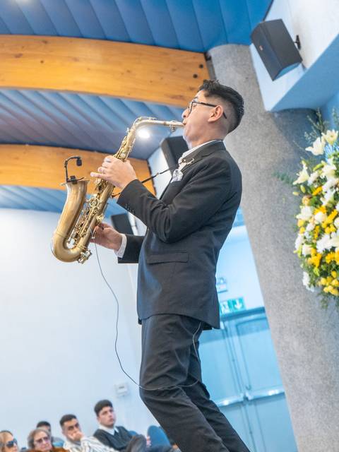 Un joven tocando saxofón en un evento con un público atento.