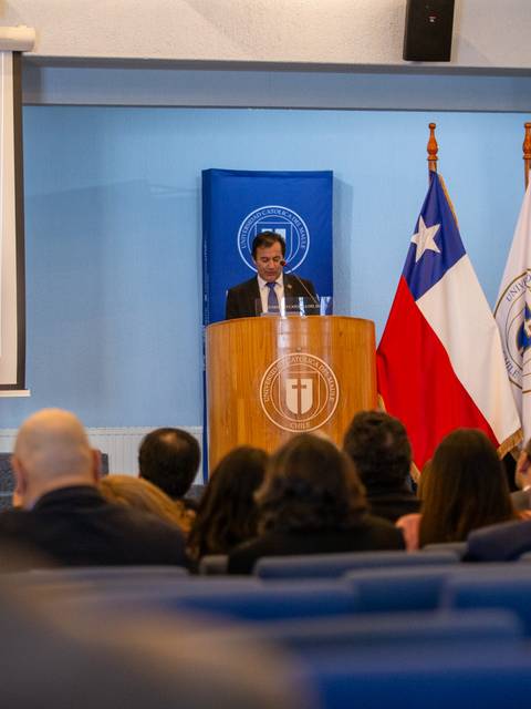 Un hombre hablando frente a un auditorio con banderas chilenas en el fondo.