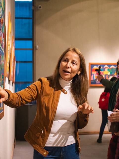 Una mujer está explicando una pintura en una galería de arte mientras otras personas la escuchan con atención.