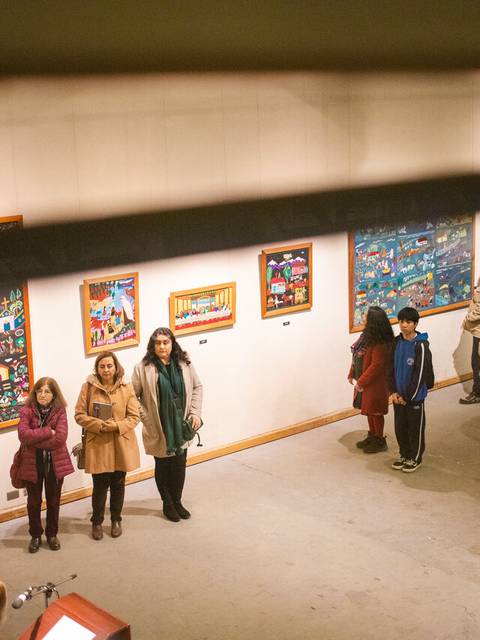 Una galería de arte con personas observando pinturas coloridas en las paredes.