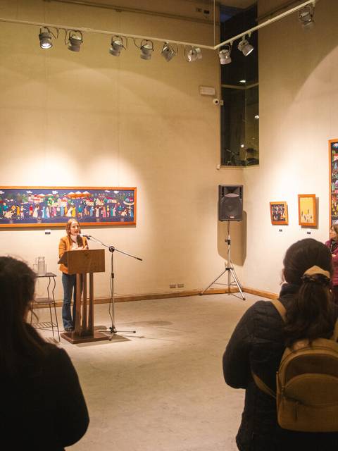 Un evento en una galería de arte con una oradora y un público atento.