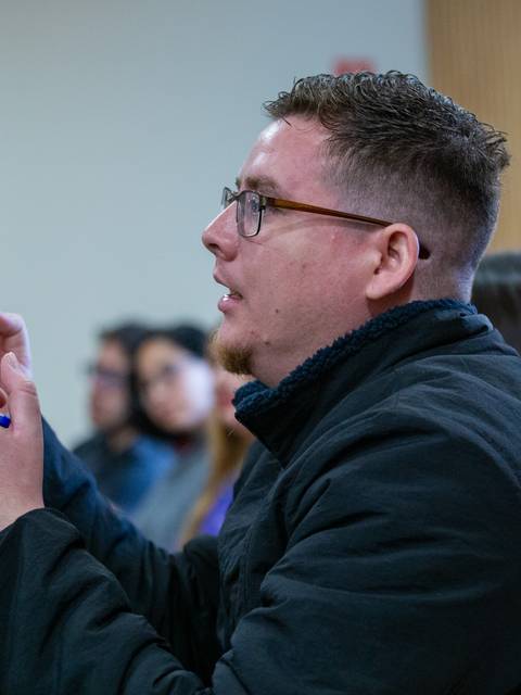 Un hombre en una charla, participando activamente y gesticulando con un bolígrafo.