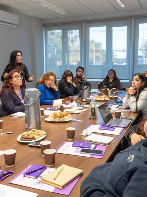 Un grupo de mujeres en una reunión, escuchando atentamente a la expositora en una sala de trabajo.