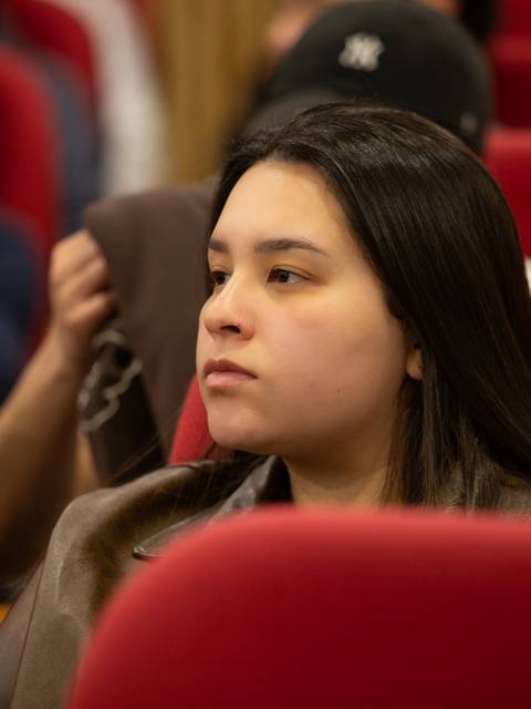 Una mujer joven escucha atentamente en una sala llena de gente.