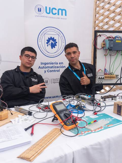 Dos estudiantes presentan su proyecto de automatización en una feria técnica.