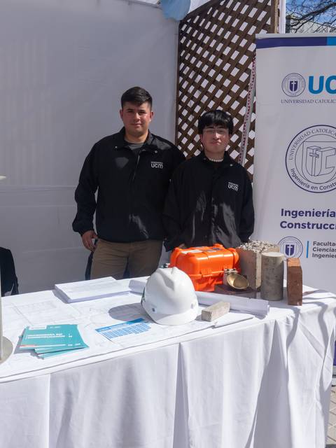 Dos estudiantes de ingeniería en construcción presentan su stand en una feria.
