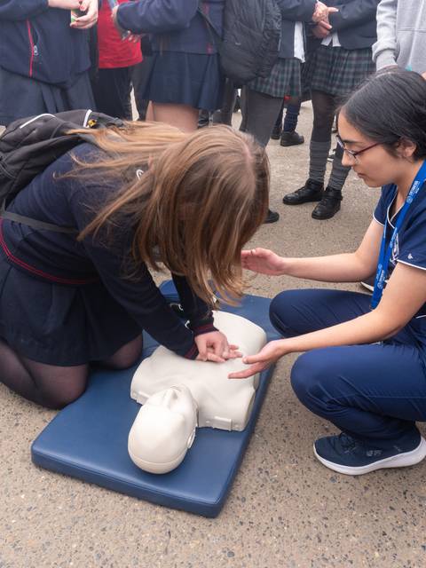 Una estudiante está practicando maniobras de RCP en un muñeco mientras una compañera le instruye.