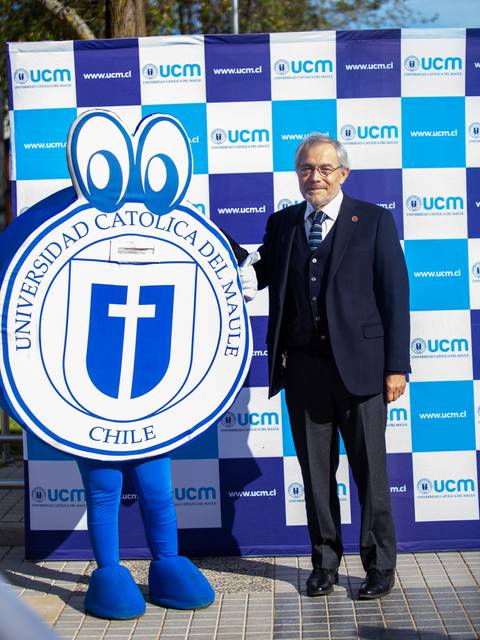 Un hombre posando junto a la mascota de la Universidad Católica del Maule en un evento al aire libre.