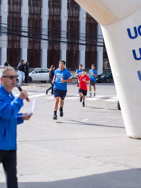 Un grupo de corredores participan en una competencia mientras un locutor anima desde el costado.