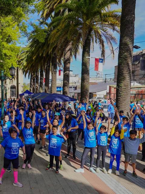 Una gran multitud de personas con camisetas azules celebra en una plaza llena de luz y árboles.