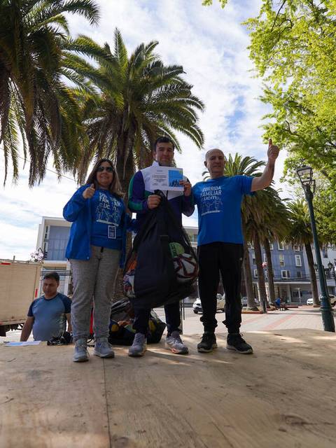 Tres personas celebran en un escenario al aire libre, rodeados de palmeras y un ambiente festivo.