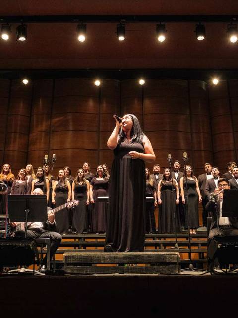 Una talentosa cantante se presenta en un escenario con una orquesta detrás en un concierto solemne.