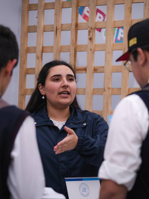 Una mujer está explicando algo a dos jóvenes en un evento educativo.