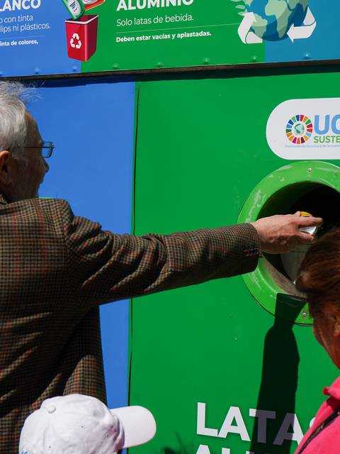 Una persona está depositando un reciclable en un contenedor de colores en un evento de reciclaje.