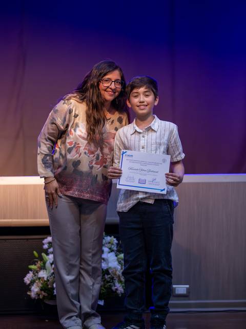 Un niño sonriente recibe un certificado junto a una mujer en un evento.