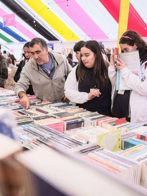 Un grupo de personas revisando libros en una feria literaria bajo un toldo colorido.