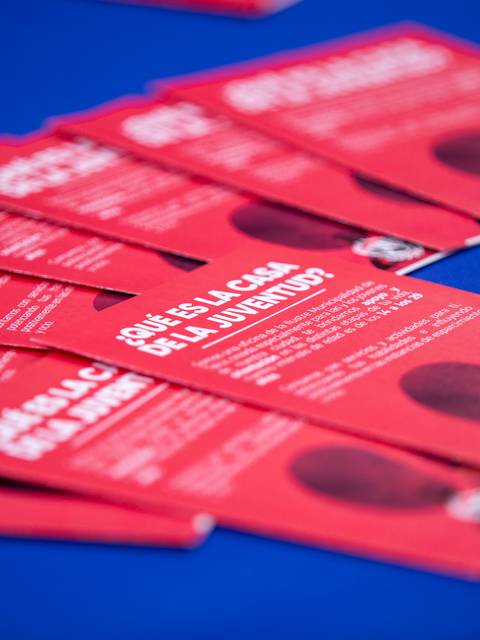 Una serie de volantes rojos apilados sobre una mesa, donde se pregunta sobre la casa de la juventud.