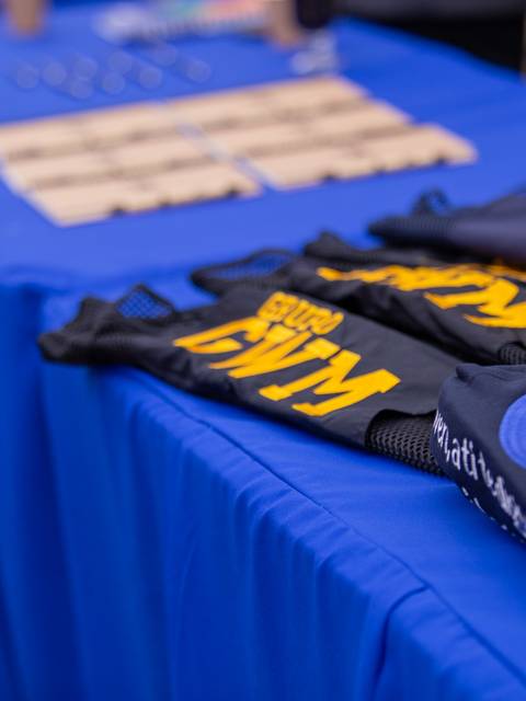 Una mesa con poleras de colores y un fondo azul en un evento al aire libre.