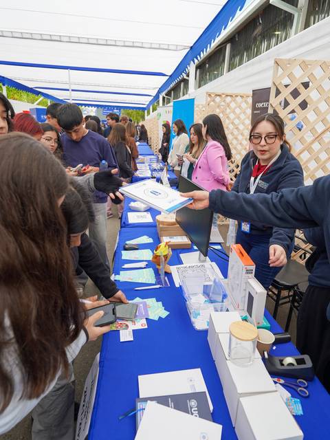 Una feria con varias personas interactuando en un stand lleno de información y productos.