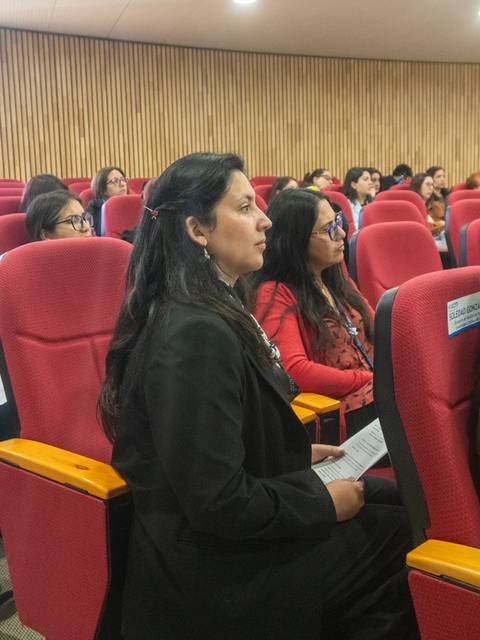 Un grupo de personas atentas en una charla mientras están sentadas en asientos rojos.