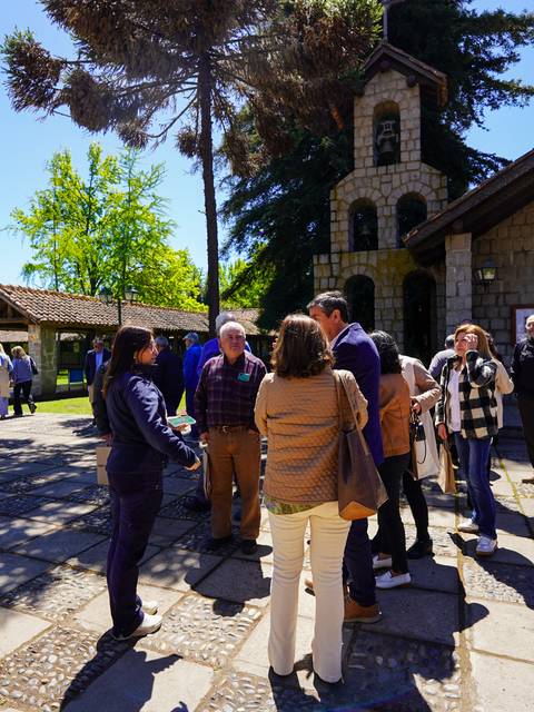 Un grupo de personas conversando en un lugar al aire libre con árboles y un edificio de fondo.
