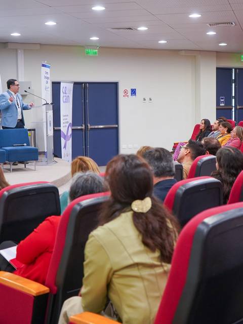 Una charla educativa en un auditorio con varias personas atentas al expositor.