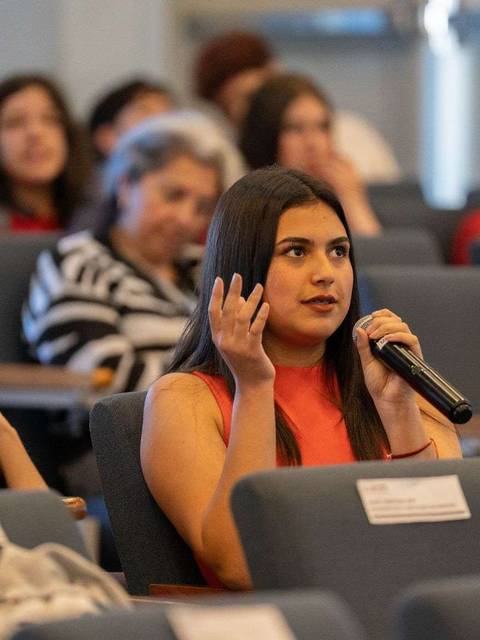 Una joven en un evento levantando la mano para hacer una pregunta.
