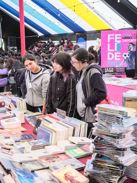 En una feria del libro, unas chicas miran entre una variedad de libros apilados.