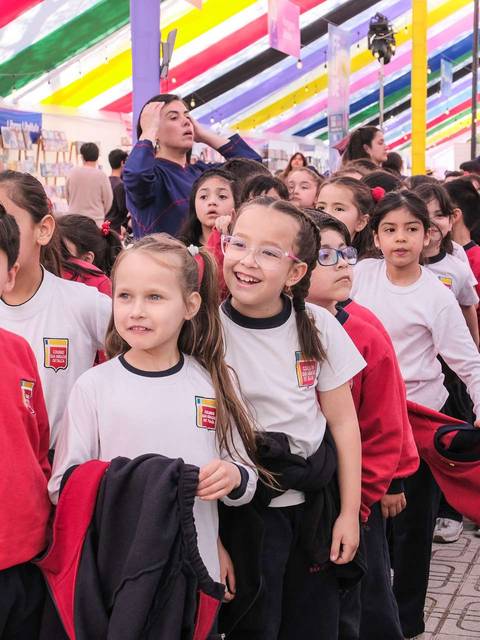 Un grupo de niños y niñas en una feria de libros, todos vestidos con uniformes escolares, disfrutando del ambiente colorido.
