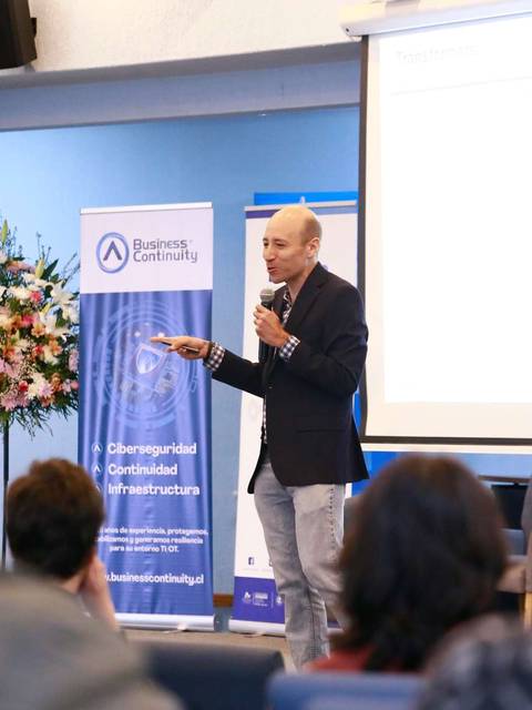 Un expositor presenta en un evento sobre ciberseguridad en un auditorio.