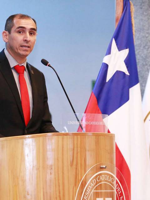 Un hombre con corbata roja está hablando en un podio frente a una bandera chilena.